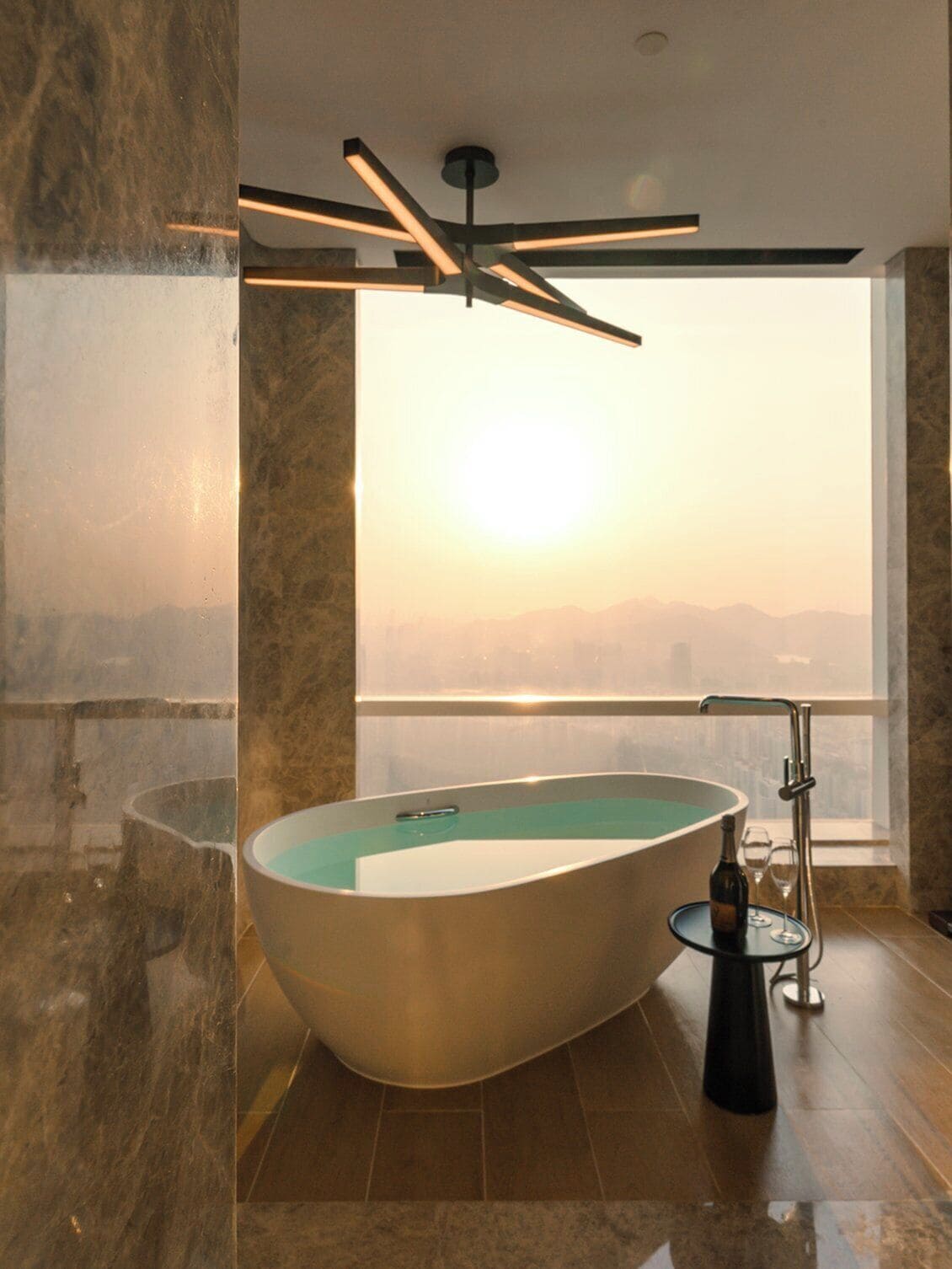Un baño moderno con una bañera independiente, una ducha con mampara de vidrio y vistas a la ciudad.
