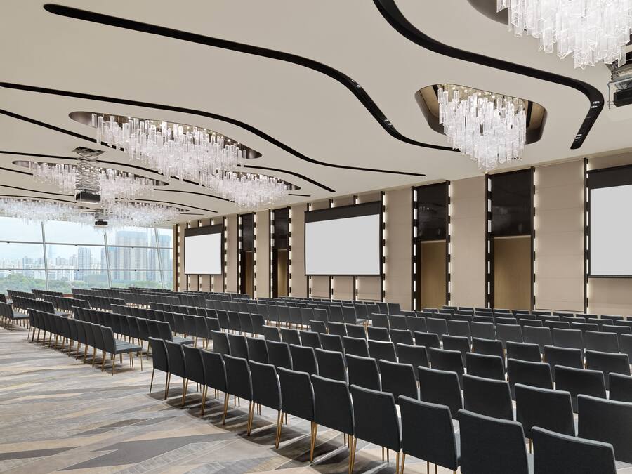 A conference room with rows of chairs, large screens, and a modern chandelier.