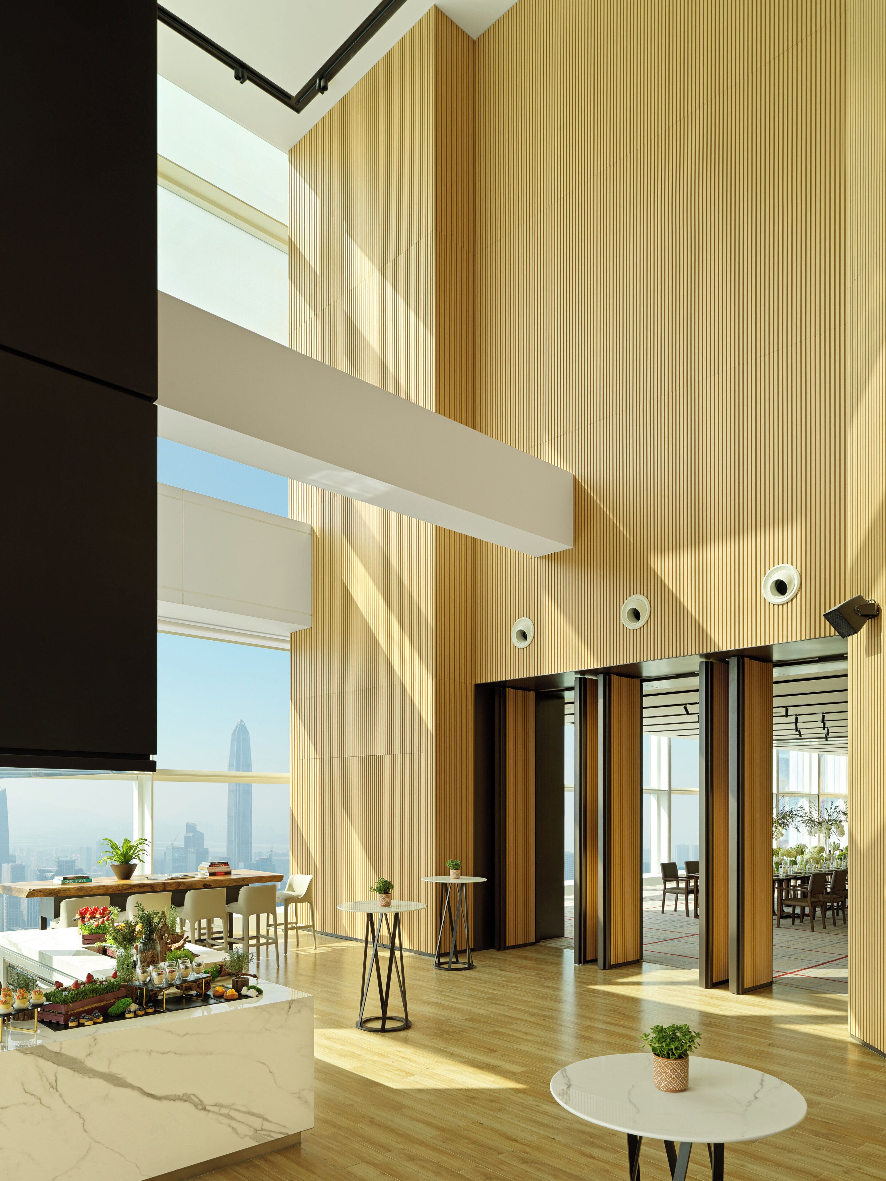 A spacious lobby with high ceilings, wooden paneling, and large windows offering a city view.