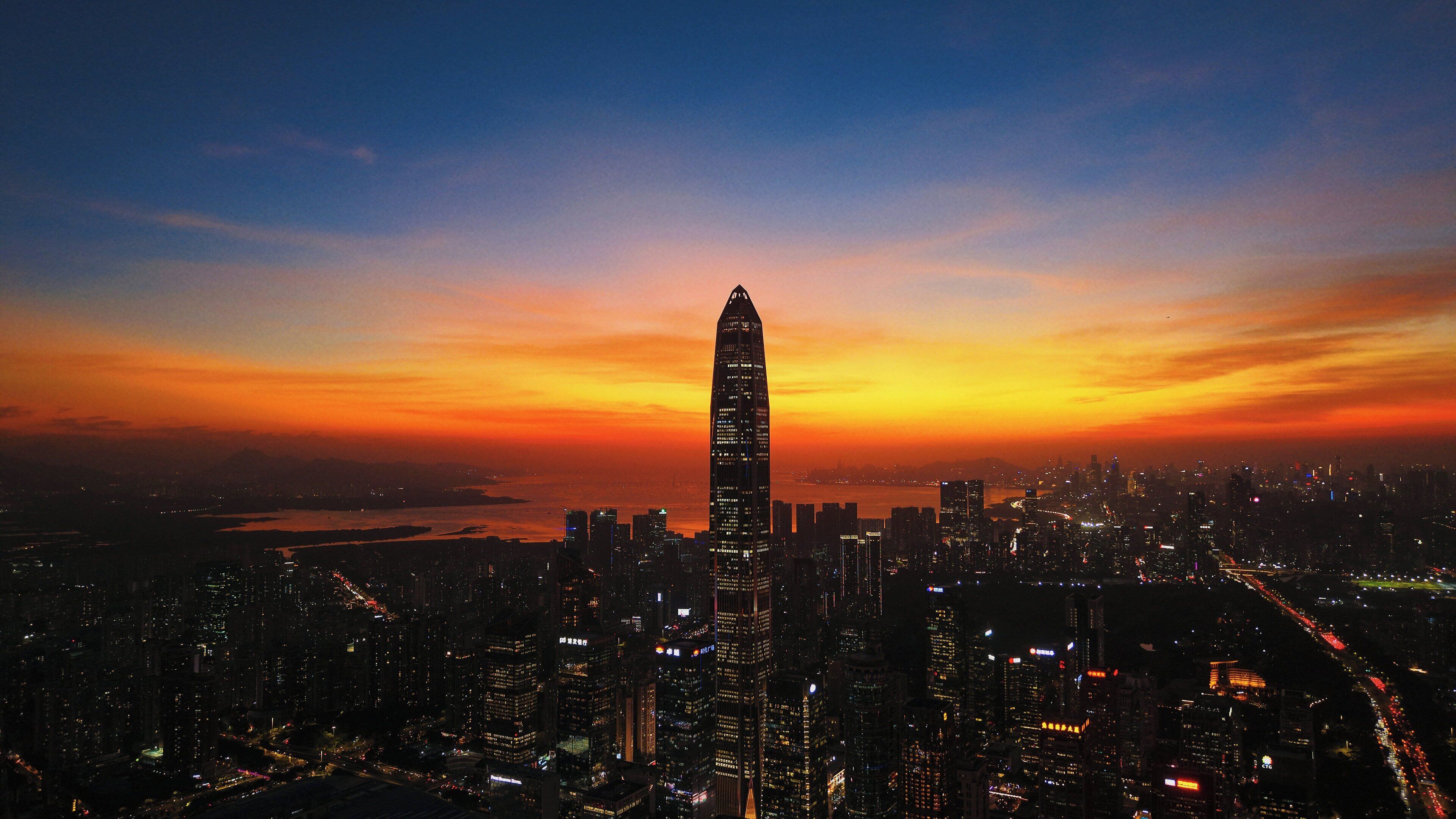 A cityscape at dusk with a prominent skyscraper in the center.