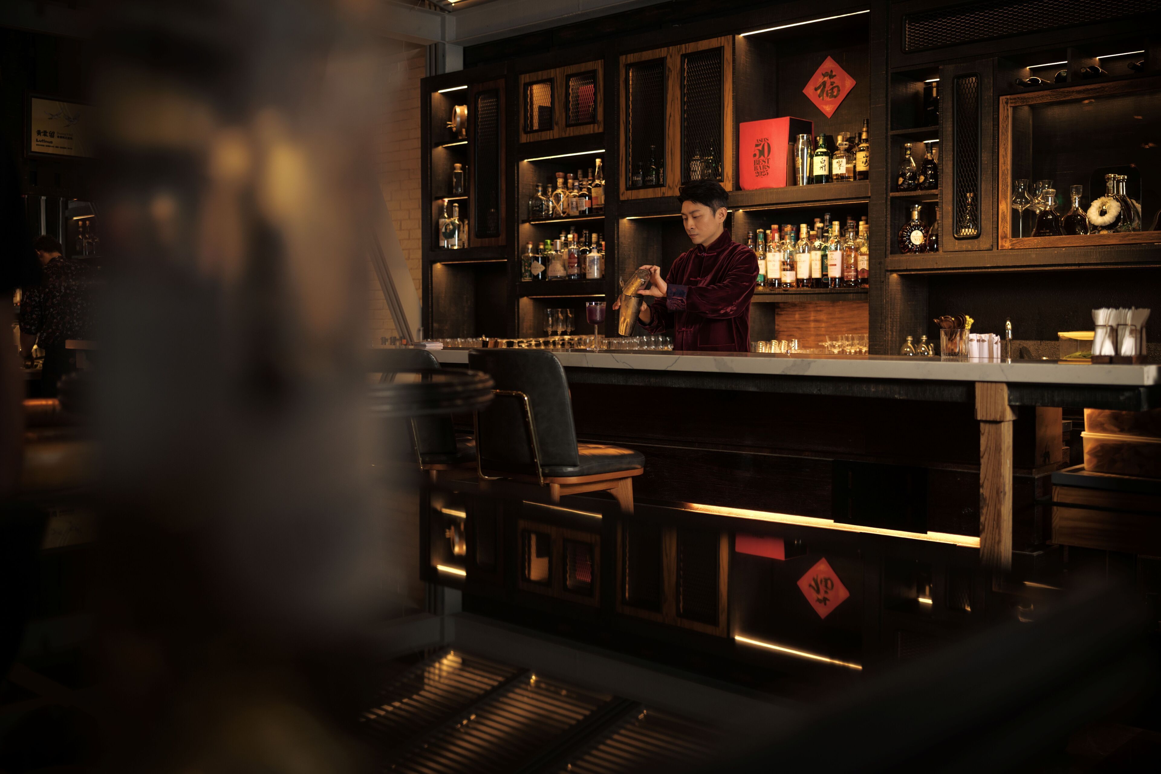 A bar area with a bartender, shelves of bottles, and a wooden counter.