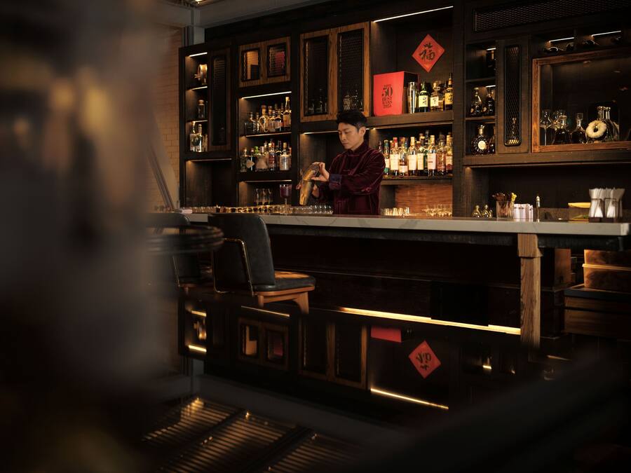 A bar area with a bartender, shelves of bottles, and a wooden counter.