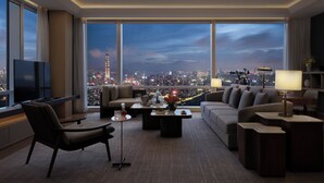 Una sala de estar moderna con vista a la ciudad, ventanas amplias, un televisor de pantalla plana y muebles contemporáneos.