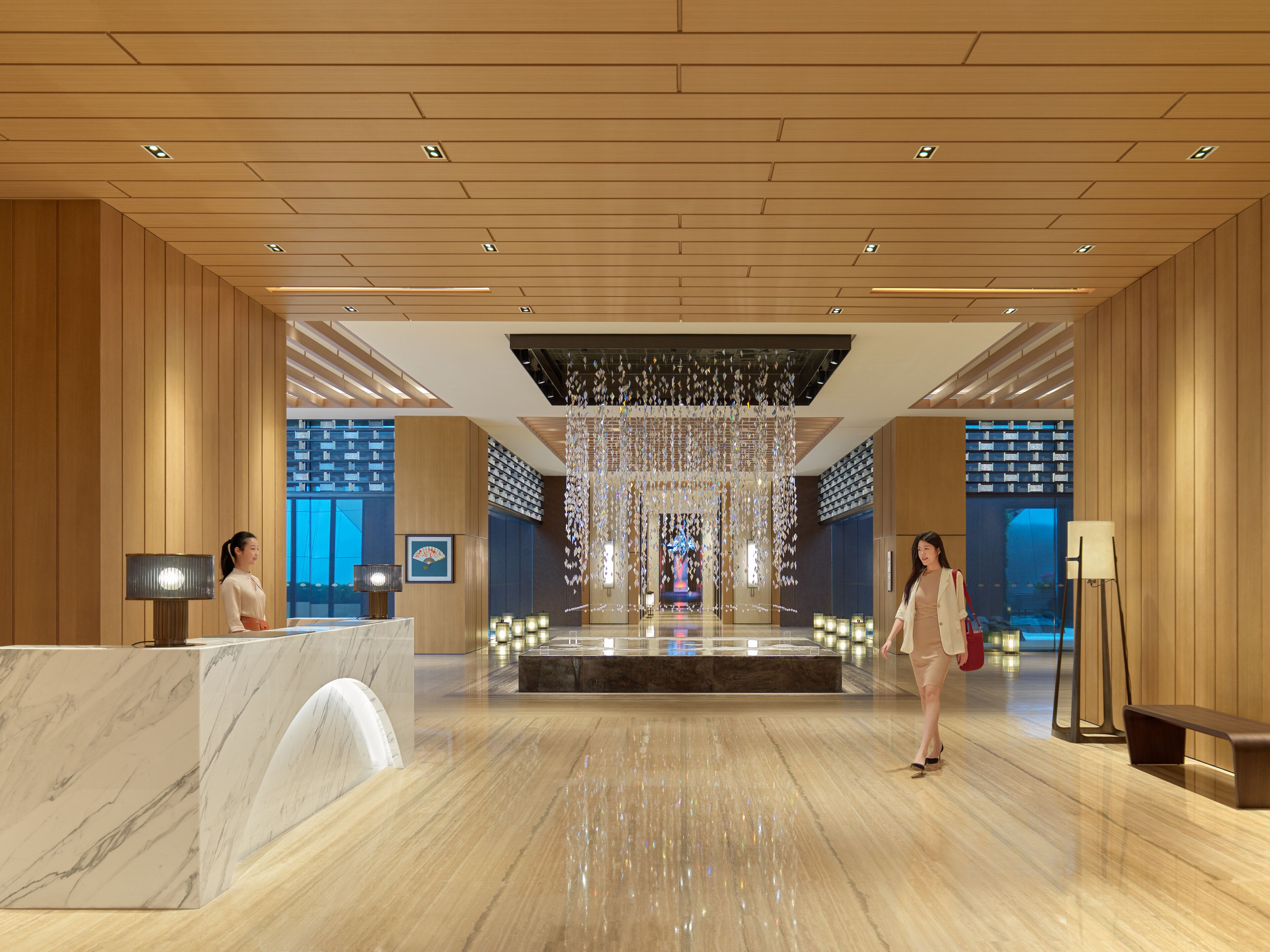 A spacious lobby with a marble reception desk, a large chandelier, and a view of the lobby through a glass wall.