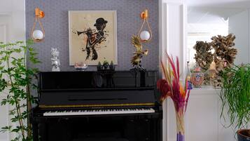 Un piano negro con un cuadro abstracto enmarcado encima, dos apliques de pared y diversos objetos decorativos, como plantas y esculturas.
