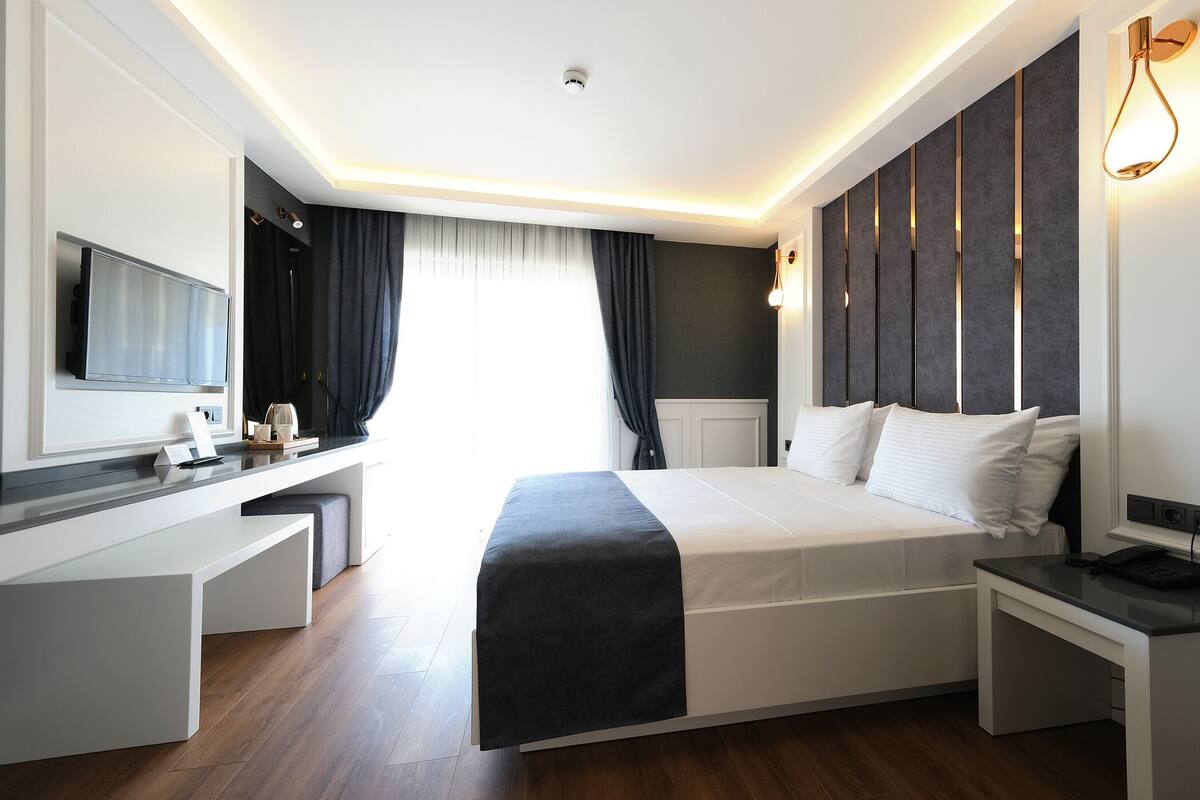 A modern hotel room with a bed, bedside table, desk, and a television.
