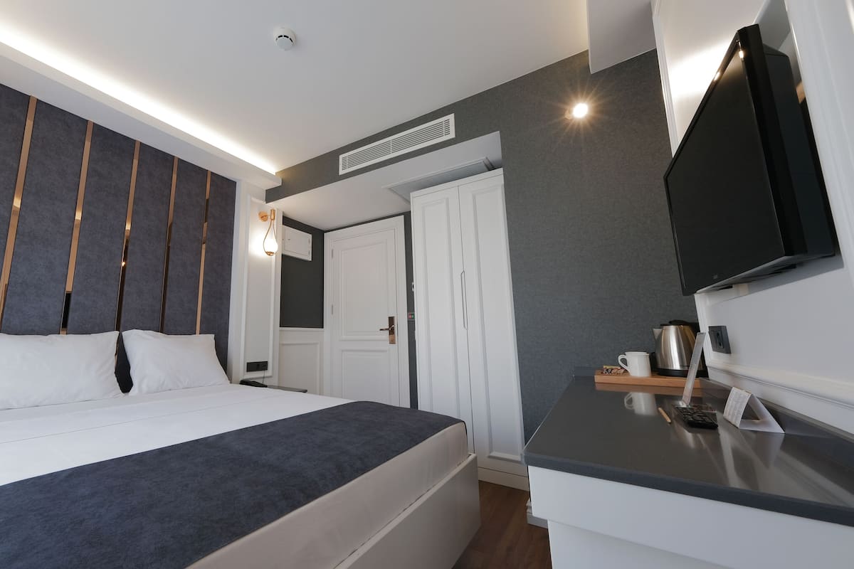 A modern hotel room with a large bed, a flat-screen TV, a desk with a coffee maker, and a wardrobe.
