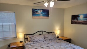 A bedroom with a bed, two bedside tables, a ceiling fan, and two wall-mounted paintings. - Charming Home- 15 mins from Historic Downtown, W+D (Savannah)