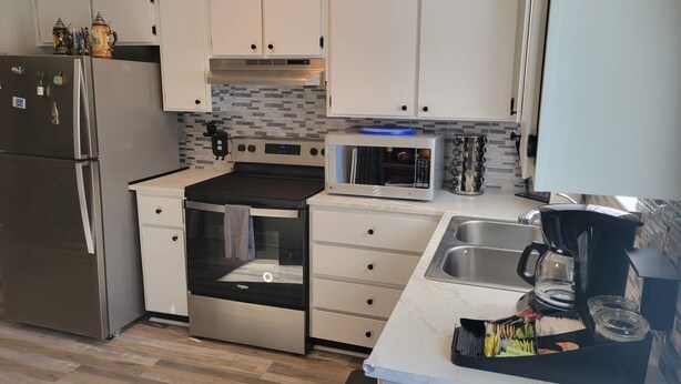 A modern kitchen with white cabinets, stainless steel appliances, a tiled backsplash, and a marble countertop. - Charming Home- 15 mins from Historic Downtown, W+D (Savannah)