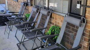 A row of outdoor lounge chairs with metal frames and cushioned seats, positioned against a brick wall with large windows and a door with a security lock. - Charming Home- 15 mins from Historic Downtown, W+D (Savannah)