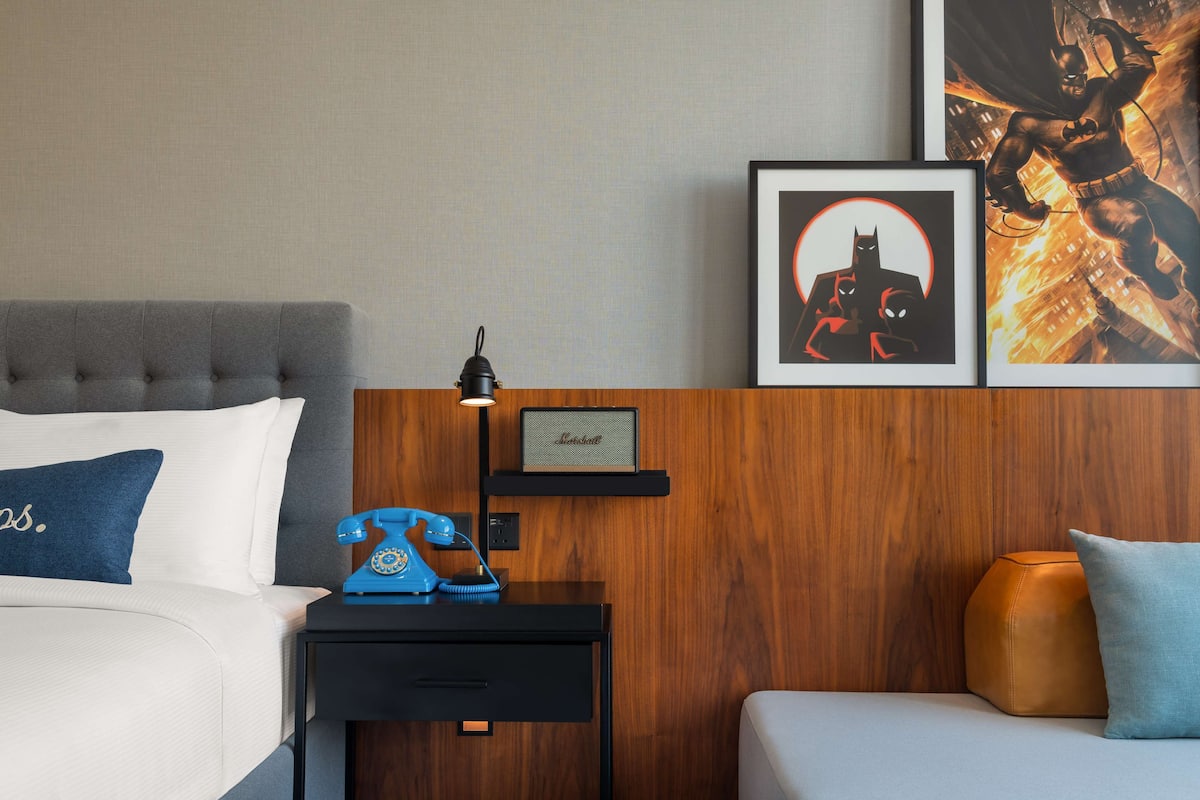 A hotel room with a bed, a nightstand with a telephone, a framed picture, and a wooden headboard.