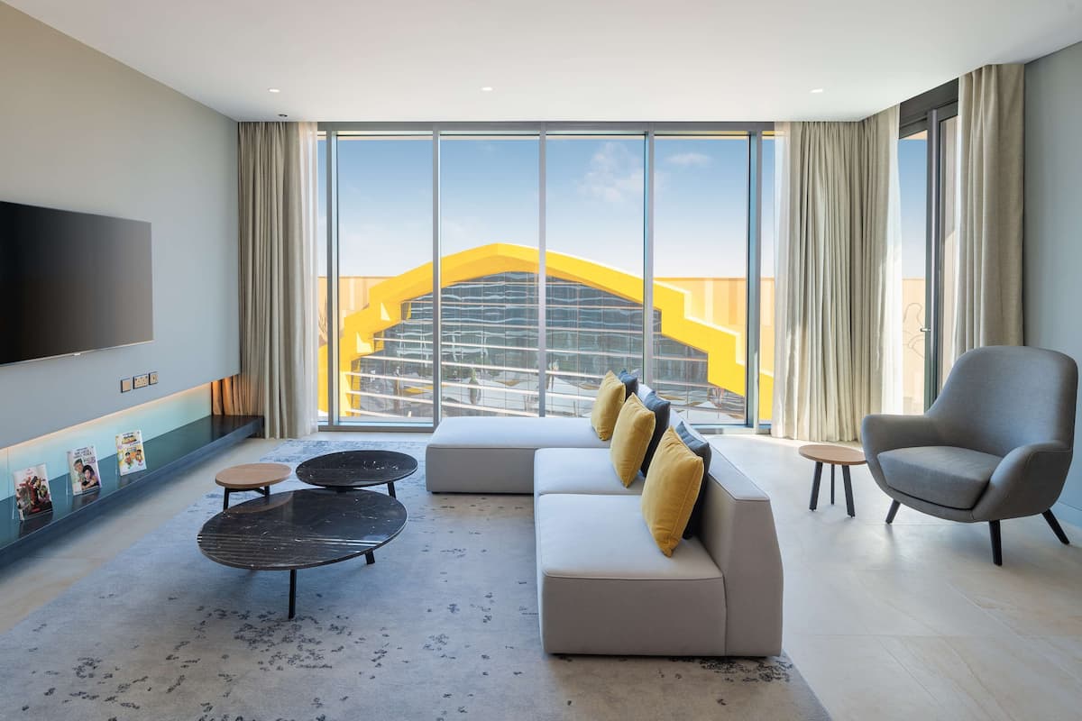 A modern living room with a large window, a flat-screen TV, a sofa, a coffee table, and a chair.