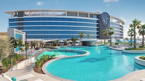 Un hotel con una piscina grande, sillas de descanso y palmeras.