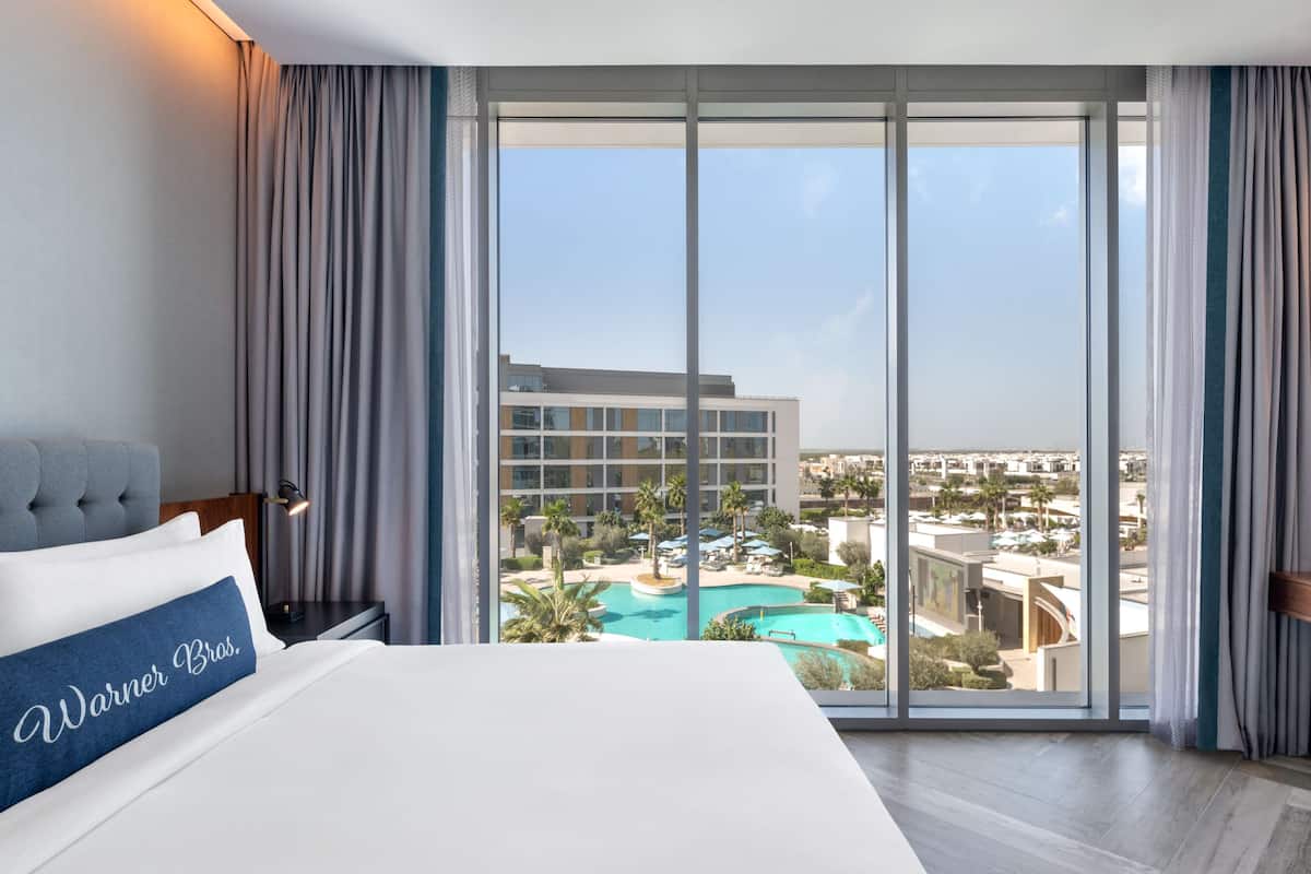 A hotel room with a large bed, a view of a swimming pool, and a cityscape.