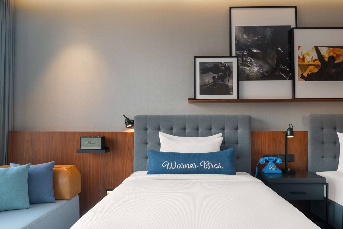 A hotel room with a large bed, a nightstand with a telephone, and framed artwork on the wall.