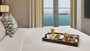 Habitación de hotel con una cama grande, una bandeja con desayuno y vistas al mar y edificios.