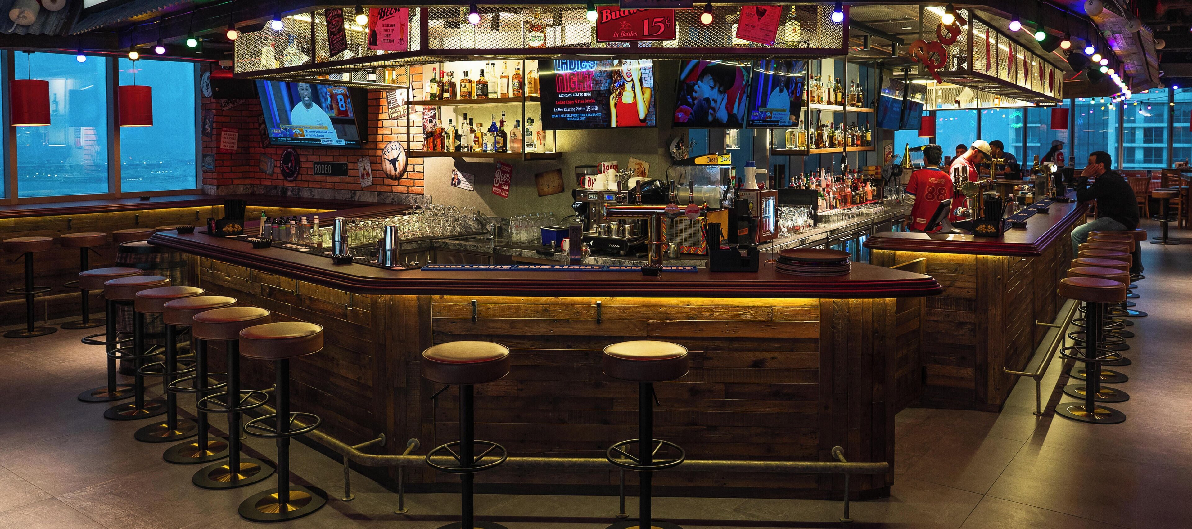 A bar area with stools, a bar counter, and a television screen.
