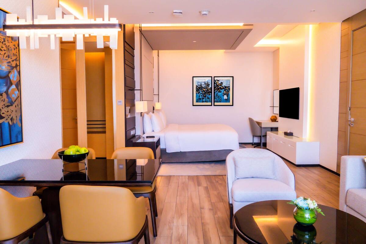 A modern hotel room with a bed, a desk, a TV, and a dining area.