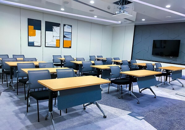 Un salón de conferencias con mesas y sillas dispuestas en filas, un proyector y una pantalla grande.