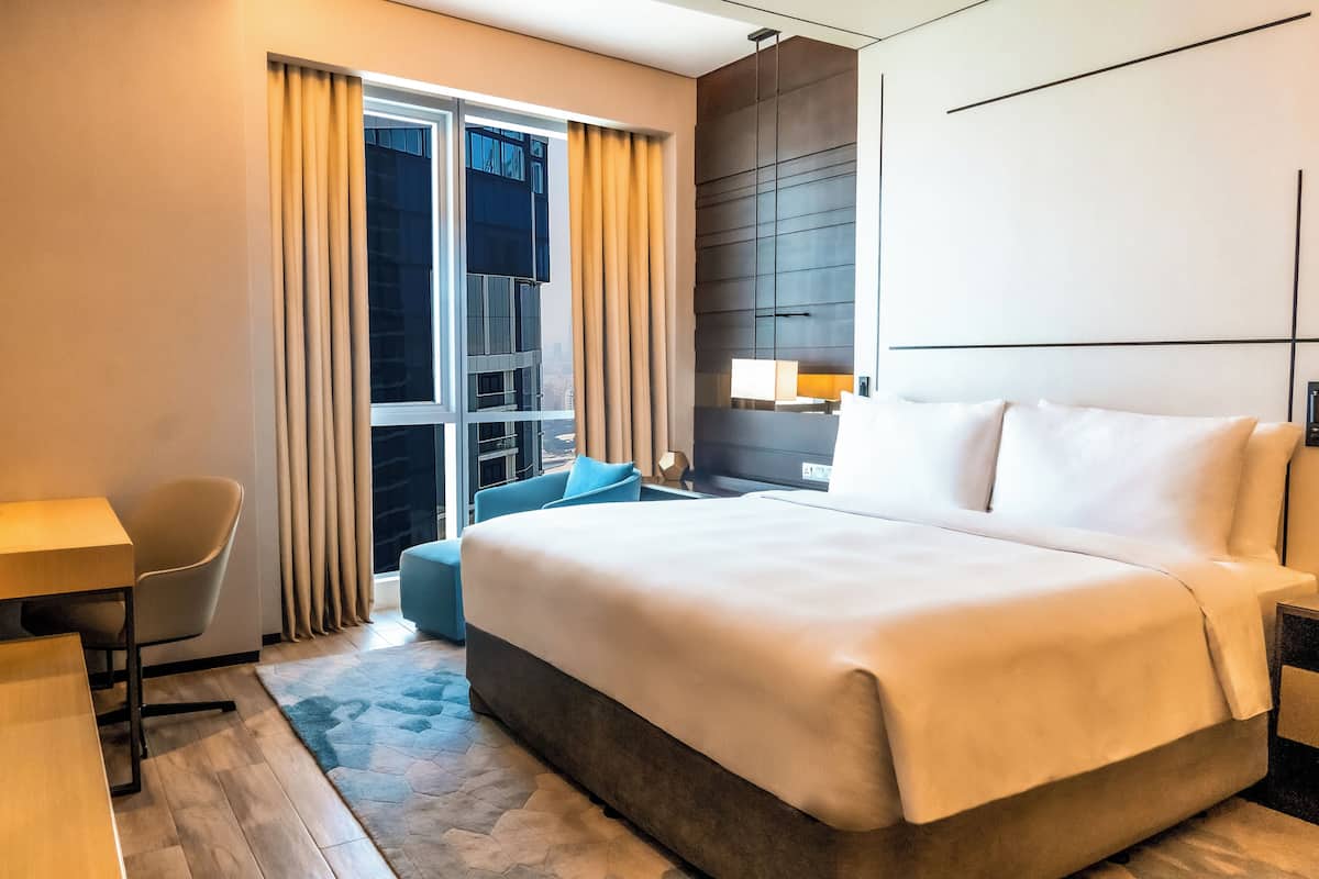 A hotel room with a large bed, a desk, a chair, a sofa, and a window with curtains.