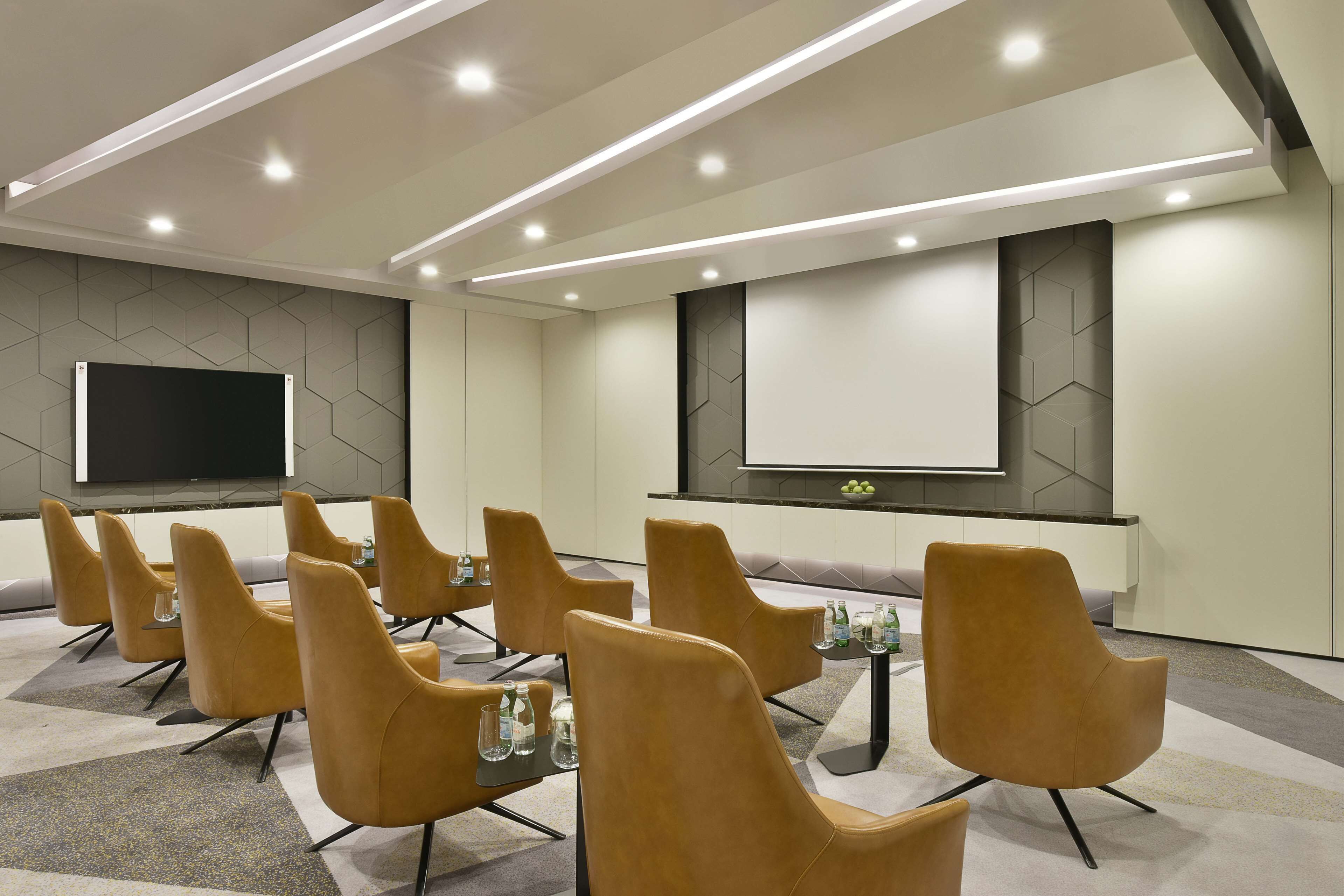 A conference room with a large screen, multiple chairs, and a carpeted floor.