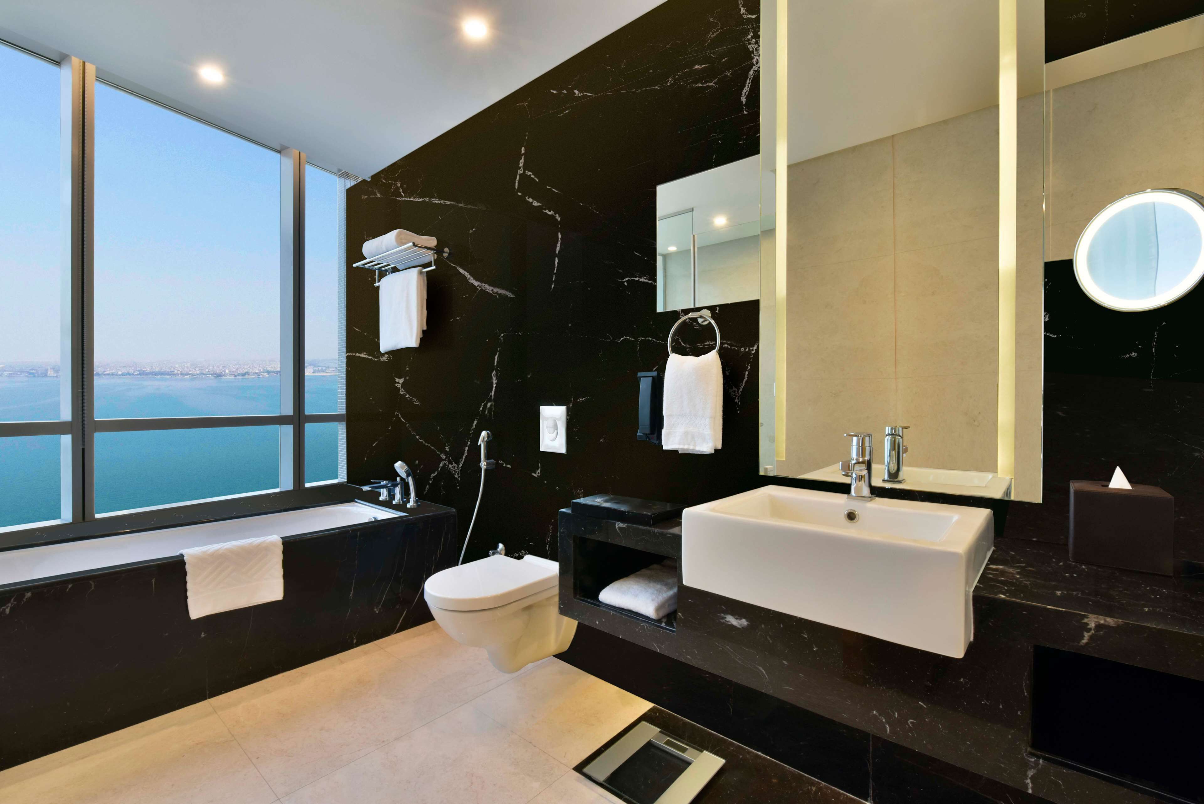 Un bany modern amb una finestra gran, una paret de marbre negre, un lavabo blanc i un vàter.