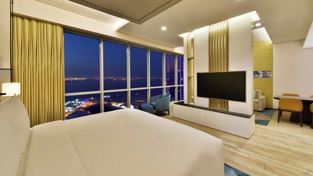 Habitación de hotel con una cama grande, televisión, escritorio y vista nocturna de la ciudad.
