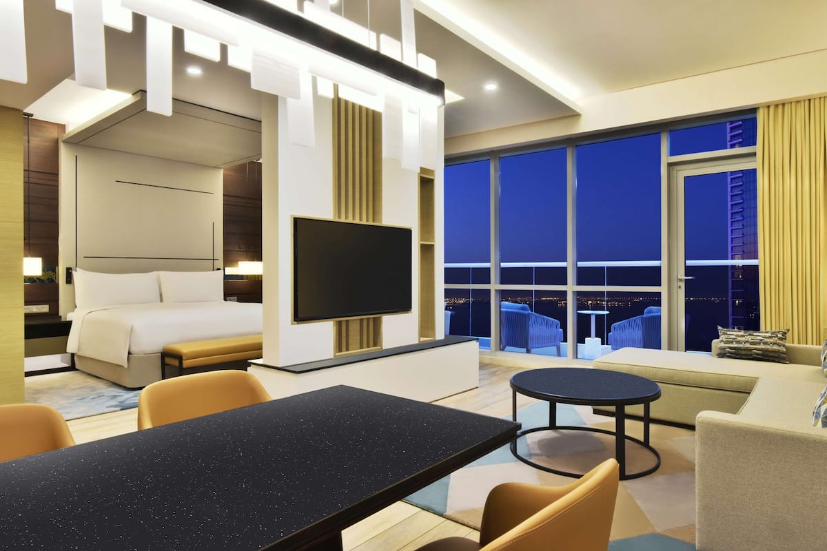 A modern hotel room with a large bed, a flat-screen TV, a dining table, and a sofa.