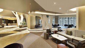 Un amplio vestíbulo con diseño moderno, que incluye una zona de estar central con sofás, sillones, una mesa de centro y un suelo estampado.