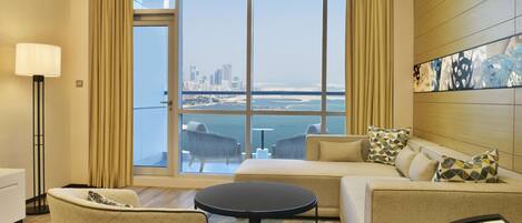 A hotel room with a large window, a sofa, a round table, and a lamp.