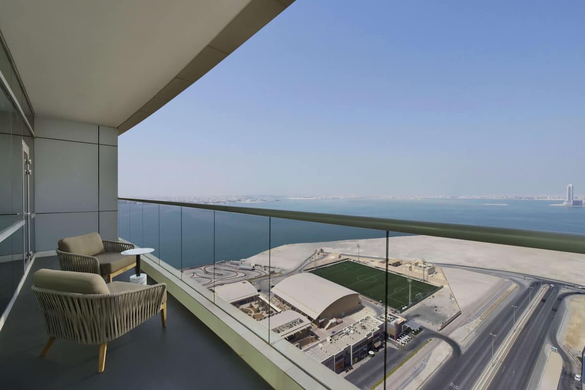 A balcony with a view of a sports complex and a coastal road.