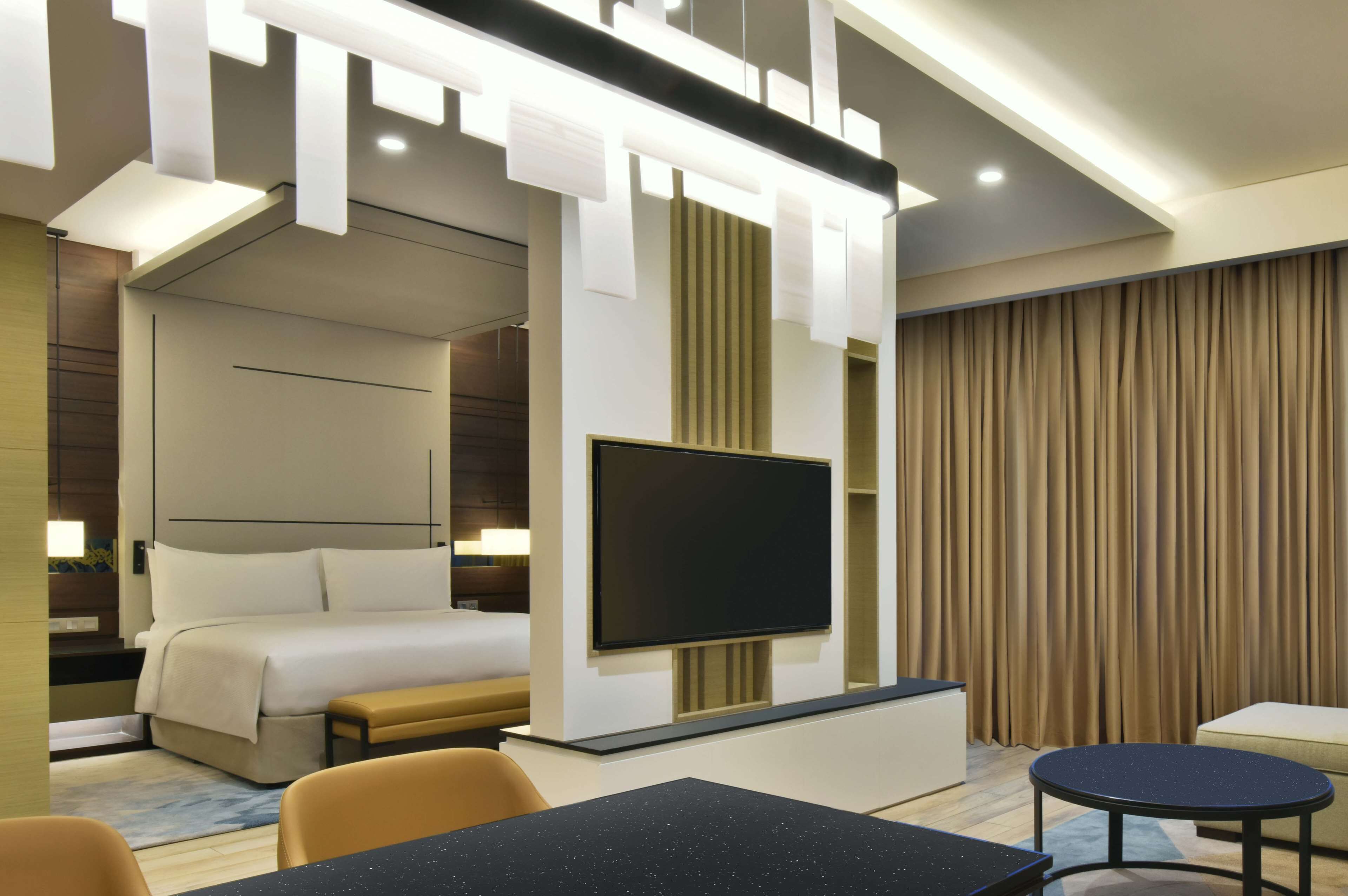 A modern hotel room with a bed, a flat-screen TV, a desk, and a seating area.