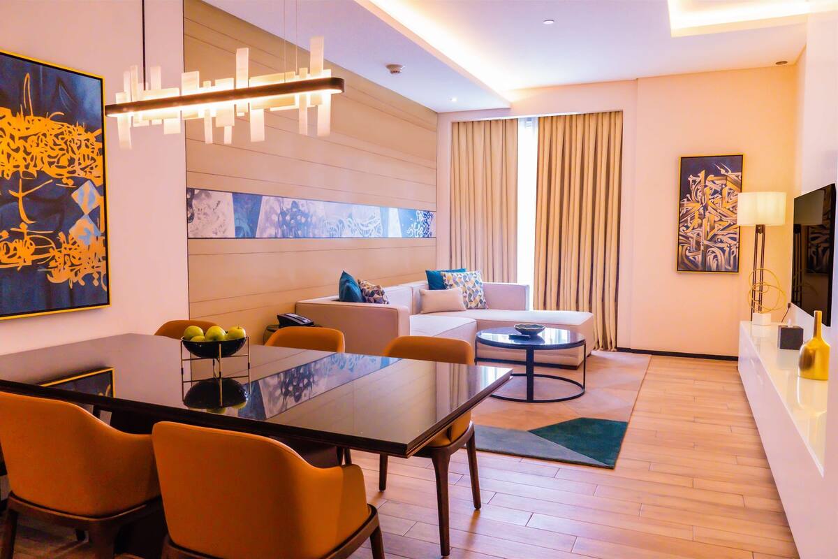 A modern hotel room with a dining area, a sofa, and a TV.