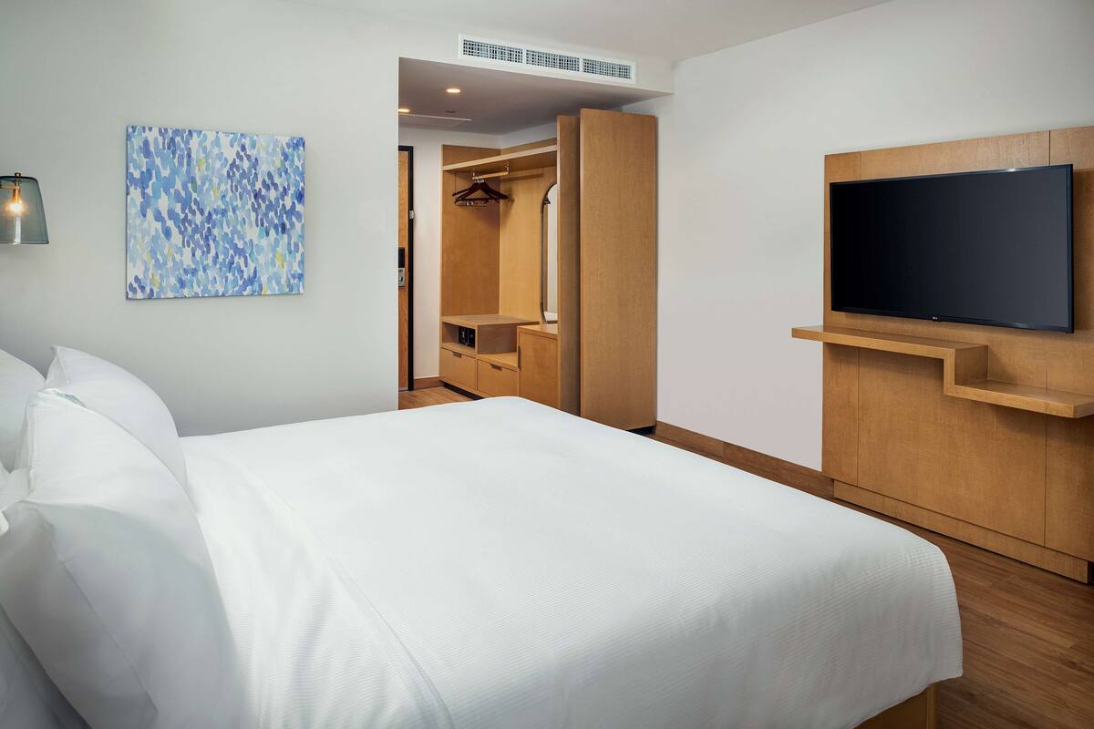 A hotel room with a bed, a TV mounted on the wall, a walk-in closet, and a painting on the wall.