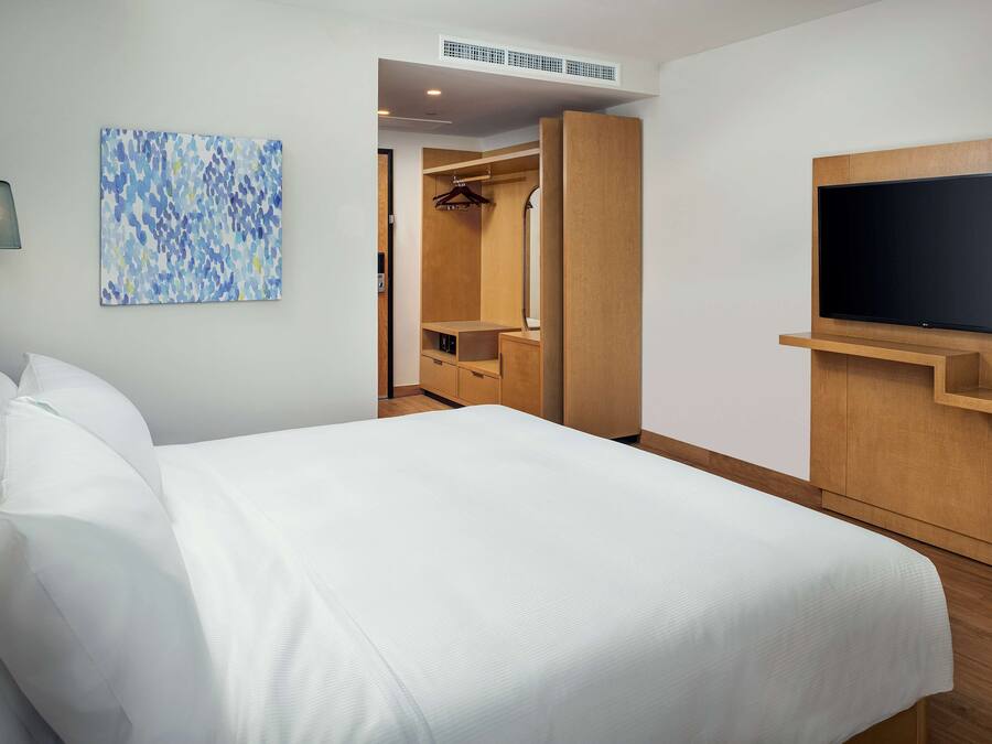A hotel room with a bed, a TV mounted on the wall, a walk-in closet, and a painting on the wall.