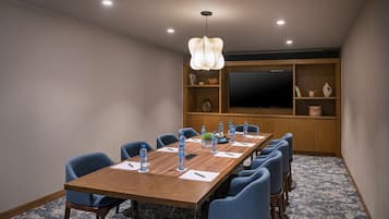 A conference room with a long wooden table, blue chairs, water bottles, and a large screen on the wall.