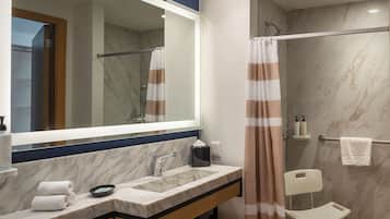 Un baño con lavamanos de mármol, espejo, toallero, cortina de ducha y una silla.
