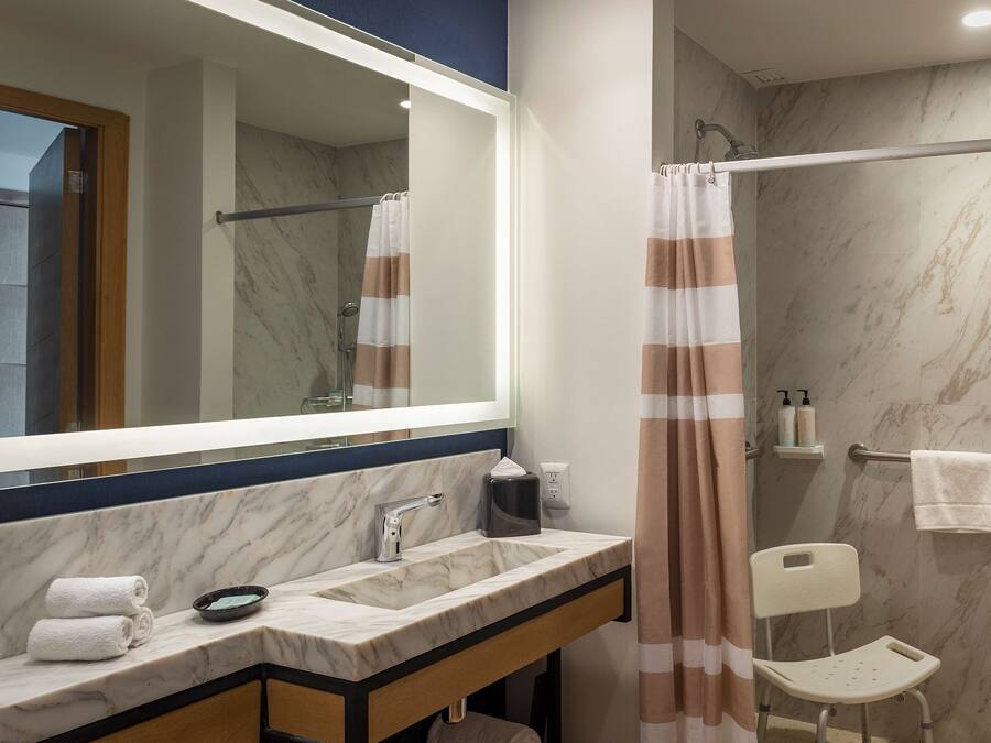 Un baño con lavamanos de mármol, espejo, toallero, cortina de ducha y una silla.