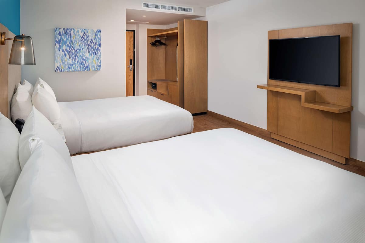 A hotel room with two beds, a TV mounted on the wall, and a walk-in closet.