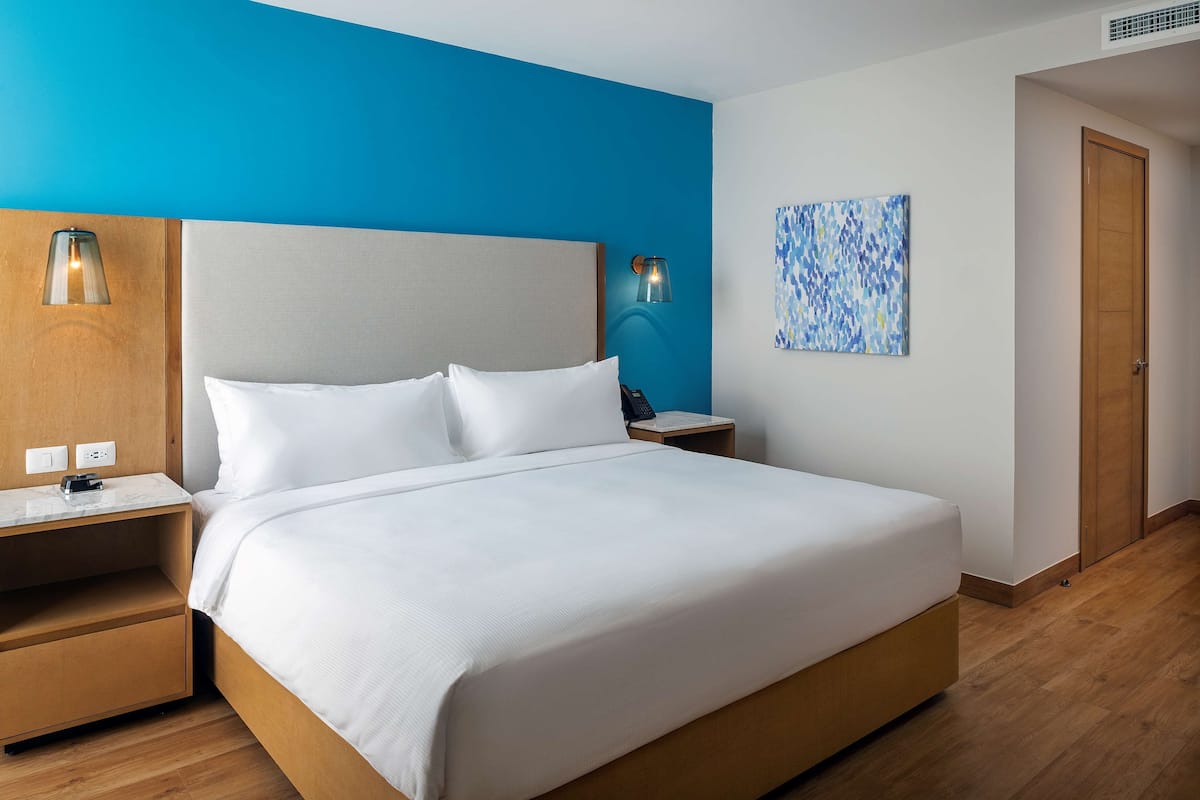 A hotel room with a large bed, wooden nightstands, a blue accent wall, and a painting.