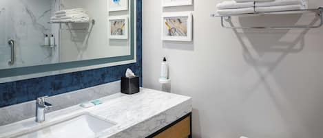 A modern bathroom with a marble sink, a large mirror, a towel rack, and framed artwork on the wall.