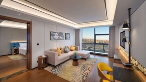 Une chambre d’hôtel moderne dotée d’une grande fenêtre donnant sur la ville, d’un canapé avec des coussins, d’une petite table d’appoint et d’un bureau avec une chaise.