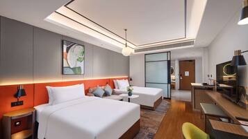 A modern hotel room with a large bed, a smaller bed, a desk, and a chair. There is a painting on the wall, a lamp, and a window.