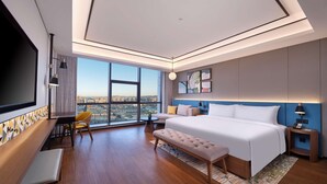 Une chambre d’hôtel moderne dotée d’un grand lit, d’un bureau avec une chaise, d’un banc, d’une télévision et d’une grande fenêtre donnant sur la ville.