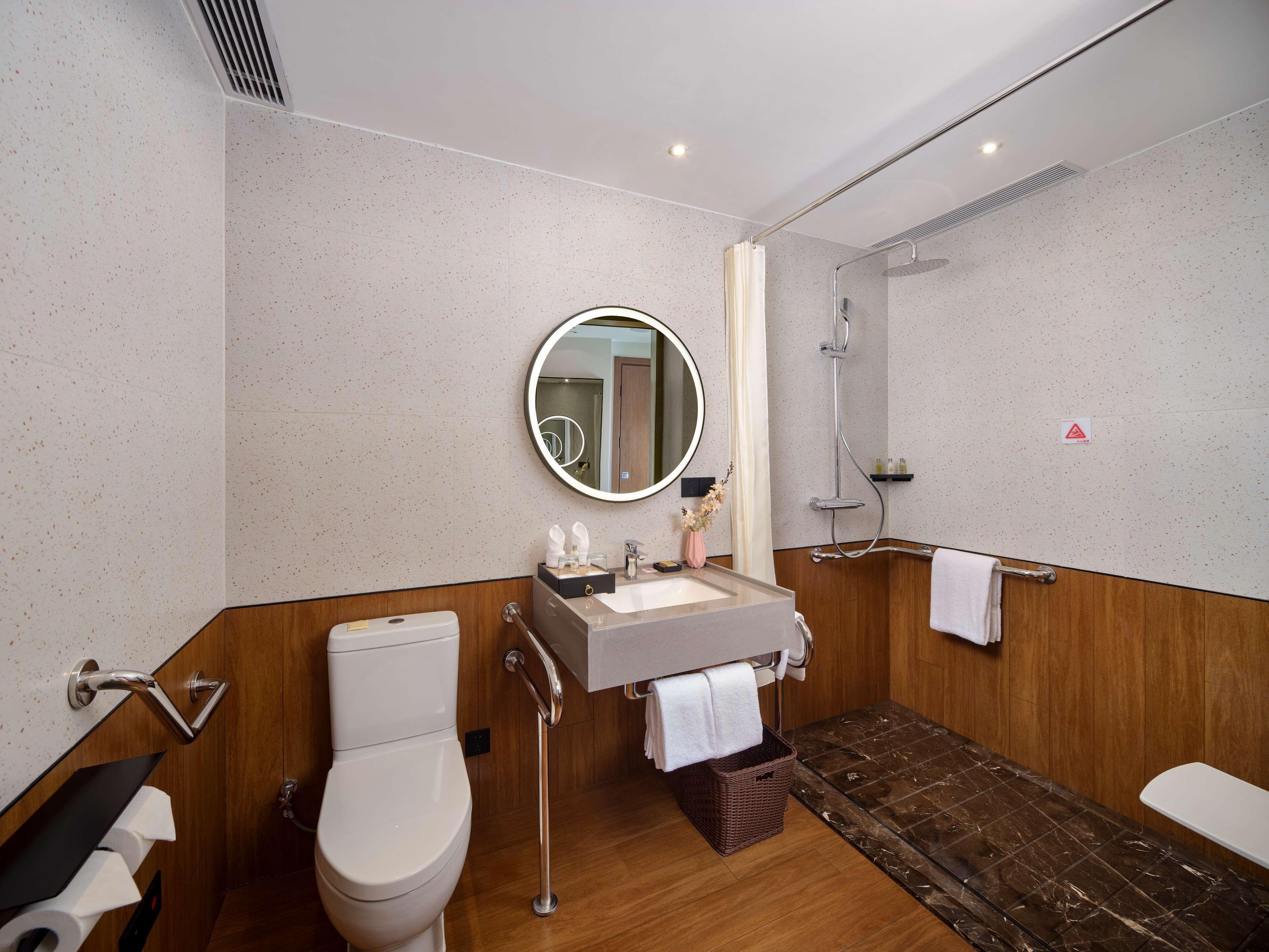 Een moderne badkamer met toilet, wastafel, spiegel, douche en een houten vloer.