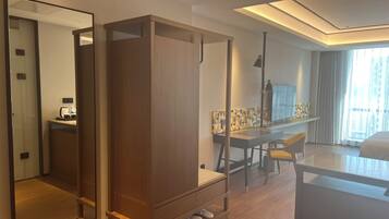 Een moderne hotelkamer met een houten garderobe, een bureau met stoel, een grote spiegel en uitzicht op de stad vanuit het raam.
