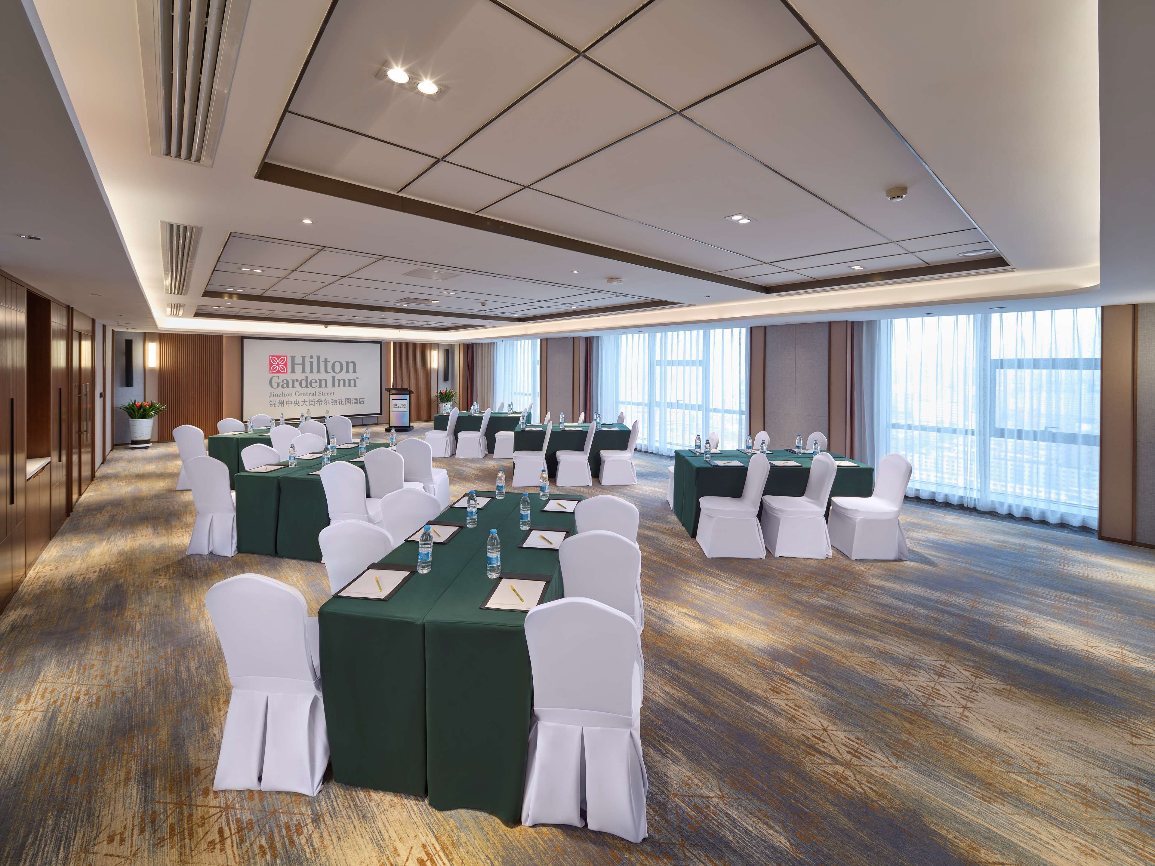 A conference room with green tables and white chairs, large windows, and a Hilton Garden Inn sign.
