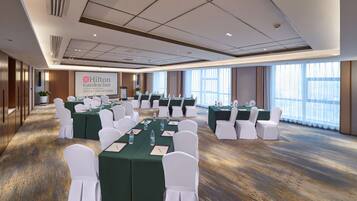 Une salle de conférence avec des tables vertes et des chaises blanches, de grandes fenêtres et une enseigne « Hilton Garden Inn ».