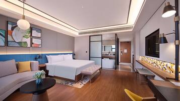 Una habitación de hotel moderna con una cama grande, un sofá, una mesa de comedor y una pequeña cocina.
