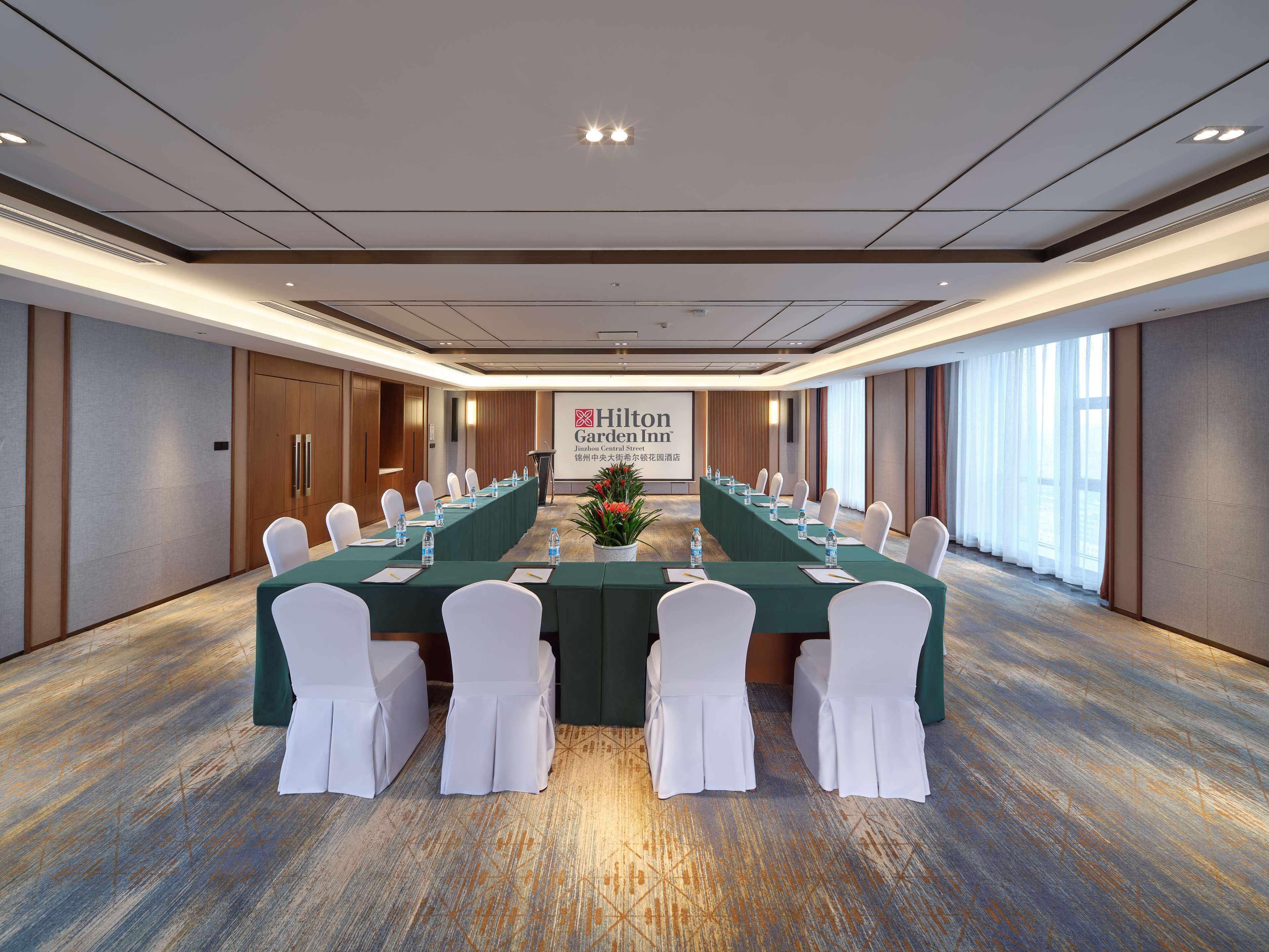Een vergaderruimte met een lange tafel, witte stoelen en een spandoek voor Hilton Garden Inn.